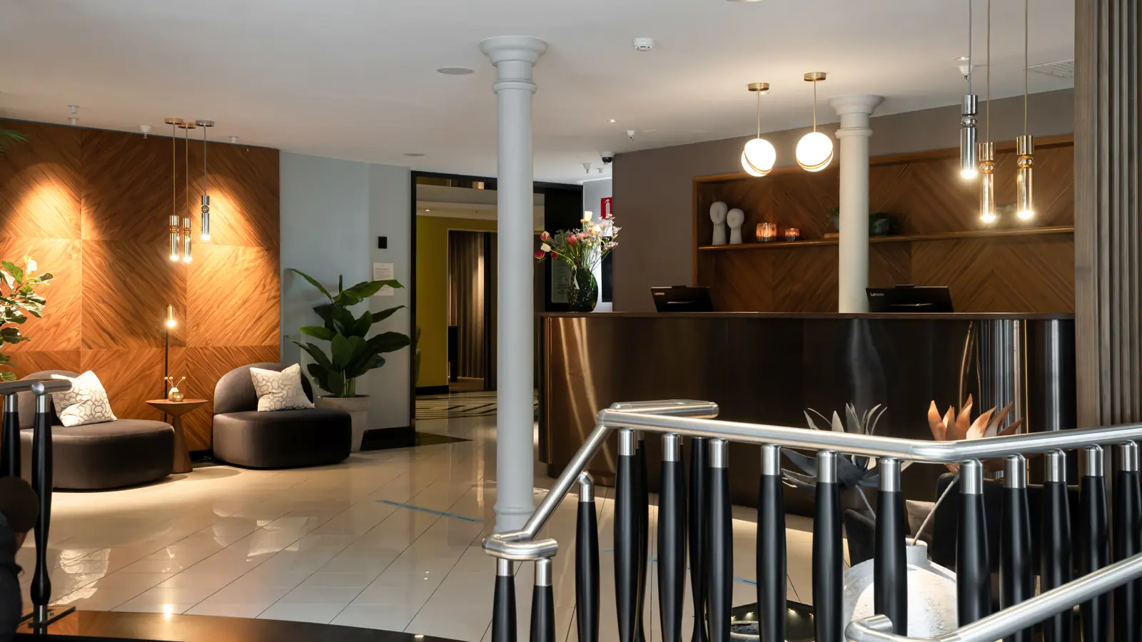 Modernt och stilrent hotellobbyområde med två svarta fåtöljer, ett litet runt träbord med en lampa, och en grön krukväxt i bakgrunden.
