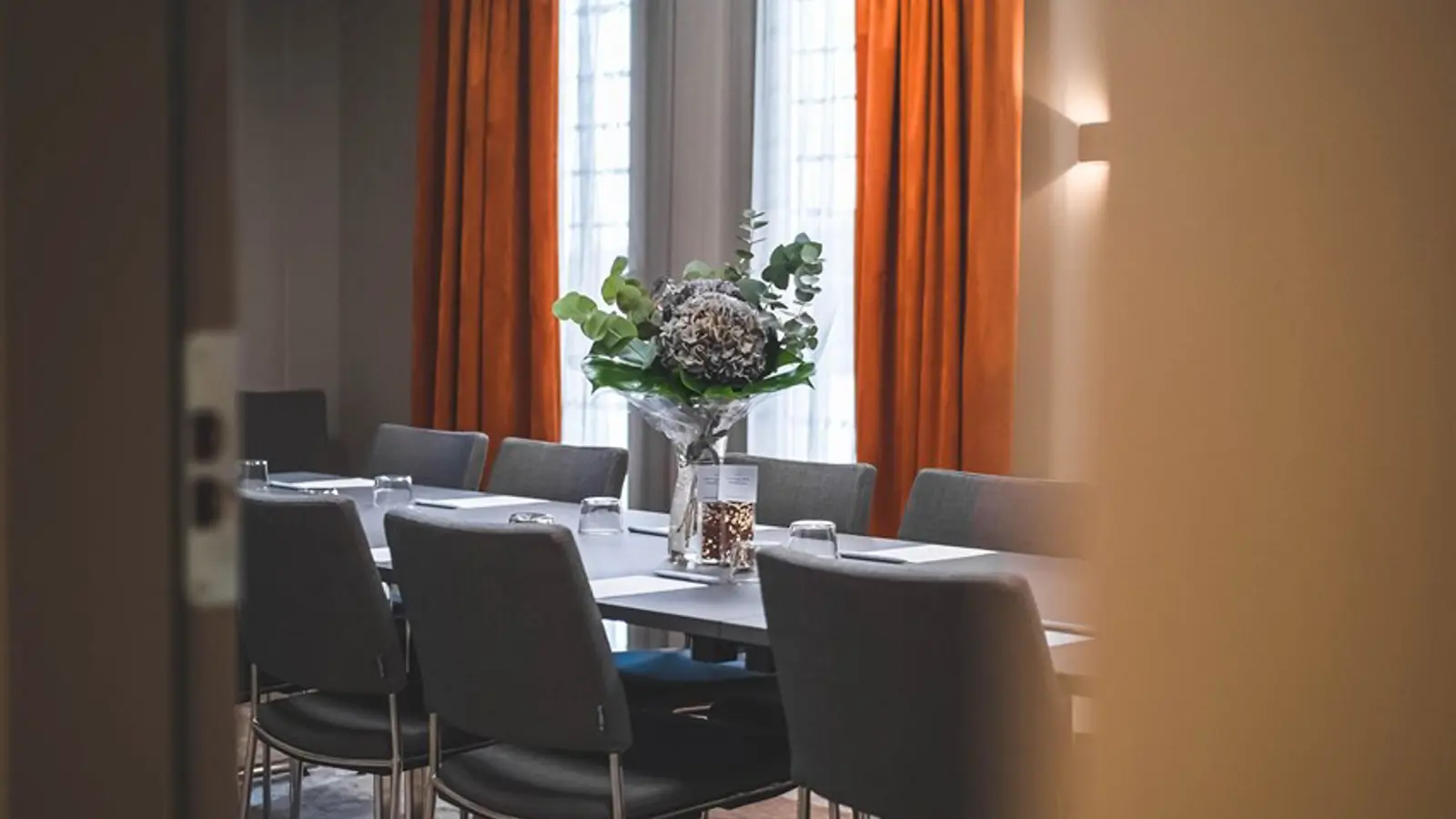Konferensrum med styrelsesittning, grå stolar och rostbruna gardiner