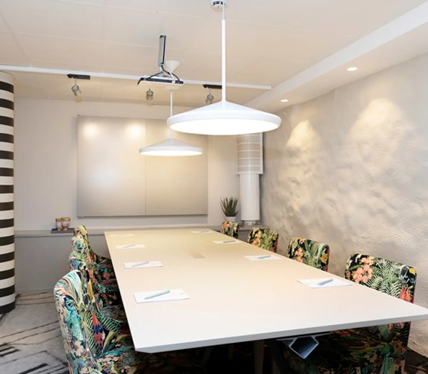 Konferensrum med styrelsesittning, vitt bord, vita väggar och mönstrade stolar