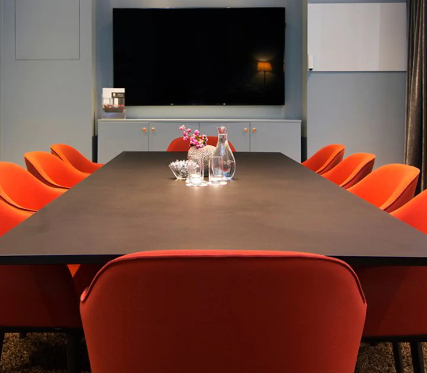 Konferensrum med styrelsesittning, brunt bord, röda stolar och blå väggar