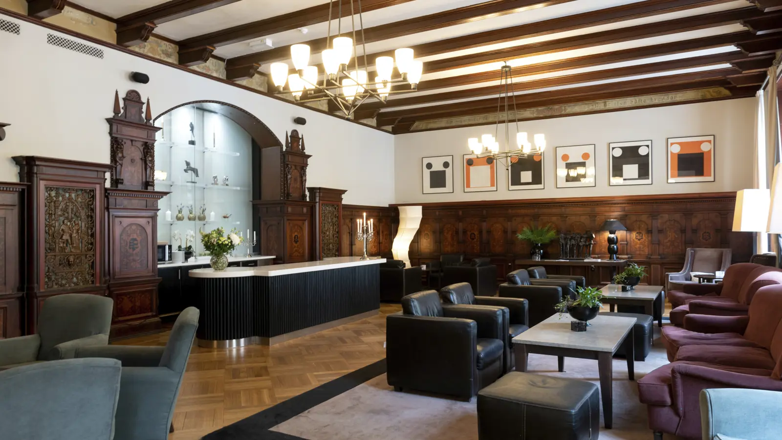 Elegant lounge med klassisk inredning, träpaneler och moderna konstverk på väggarna. Komfortabla sittplatser med fåtöljer och soffor i neutrala färger, samt dekorativa belysningsarmaturer i taket.