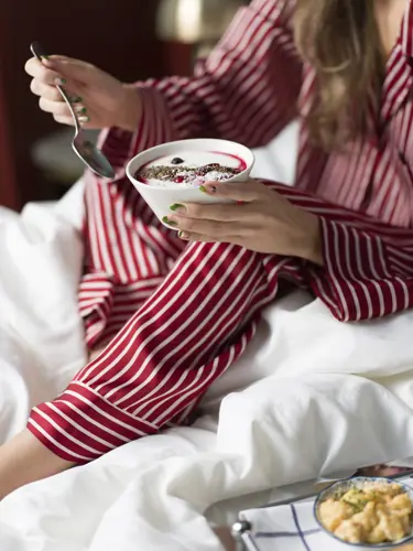 Kvinna som äter frukost i hotellsäng
